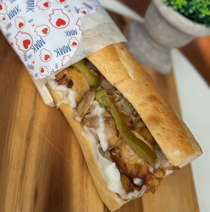 Crispy Chicken Sandwich mit Salat, Gurken und Sauce in frischem Brot auf Holzuntergrund.