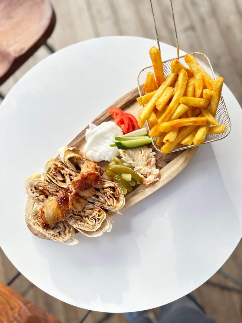 Shawarma mit Pommes, frischen Beilagen und Dips auf einem Holzbrett präsentiert.