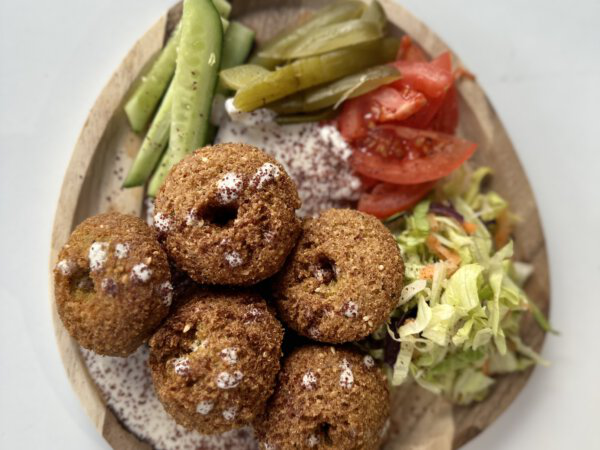 Krosse Falafelbällchen mit Gurken, Tomaten, Salat und Dips auf Holzplatte serviert.