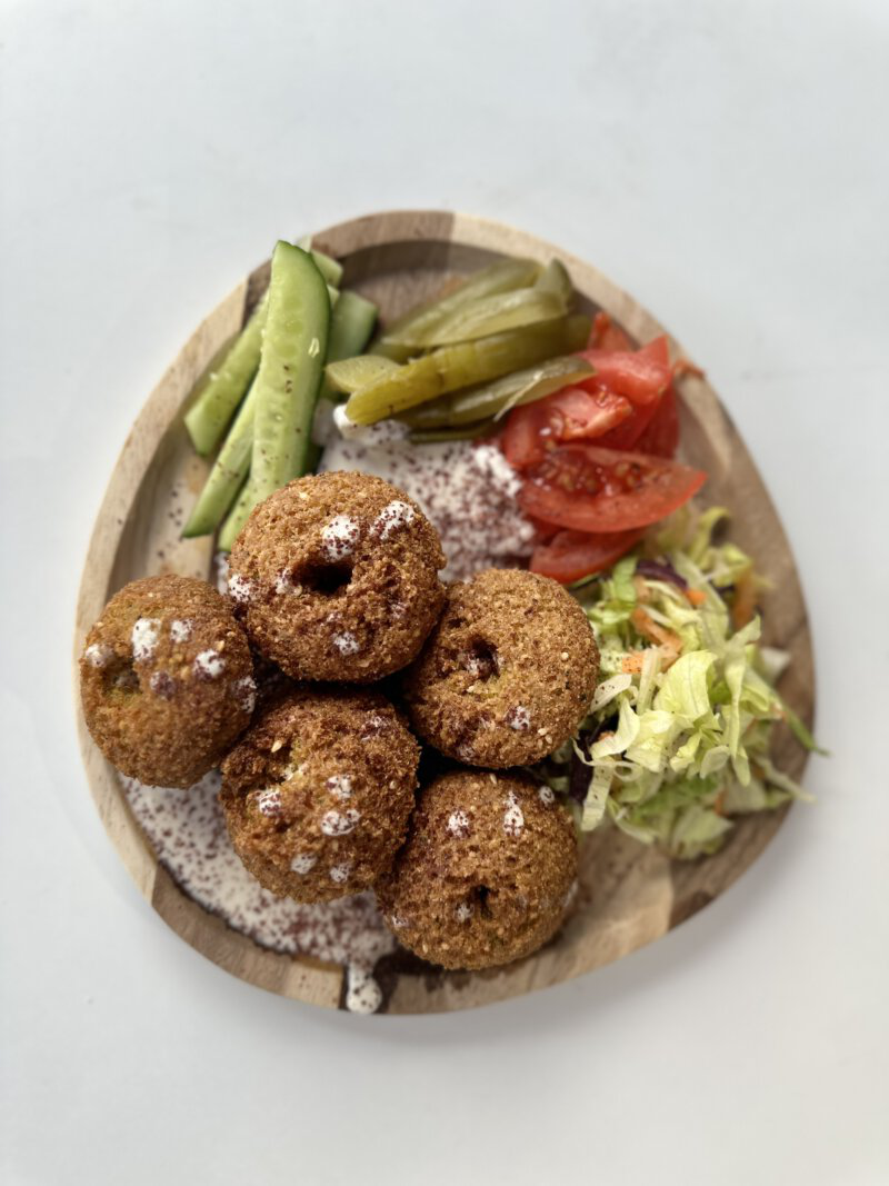 Krosse Falafelbällchen mit Gurken, Tomaten, Salat und Dips auf Holzplatte serviert.