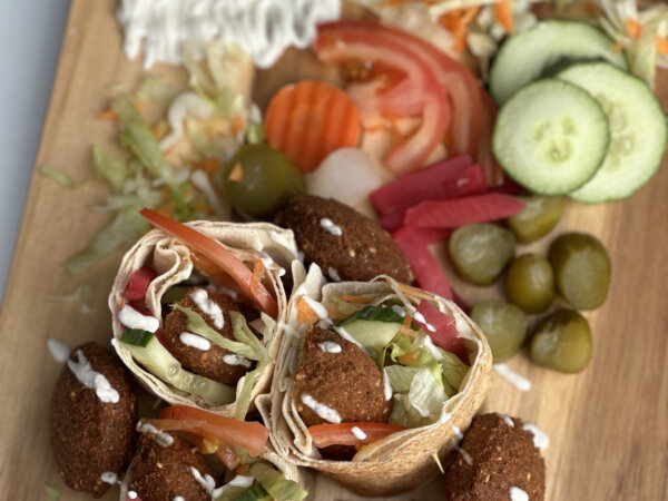 Falafel-Wraps mit frischem Gemüse, Dips und eingelegten Gurken auf Holzbrett angerichtet.