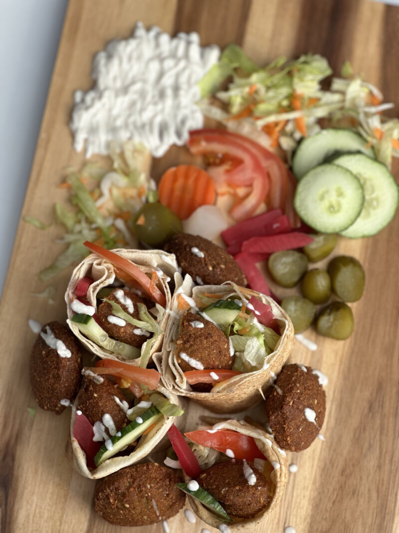 Falafel-Wraps mit frischem Gemüse, Dips und eingelegten Gurken auf Holzbrett angerichtet.