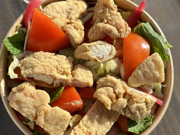 Crispy Chicken Strips in frischem Salat mit Tomaten und Gemüse in einer Schale.